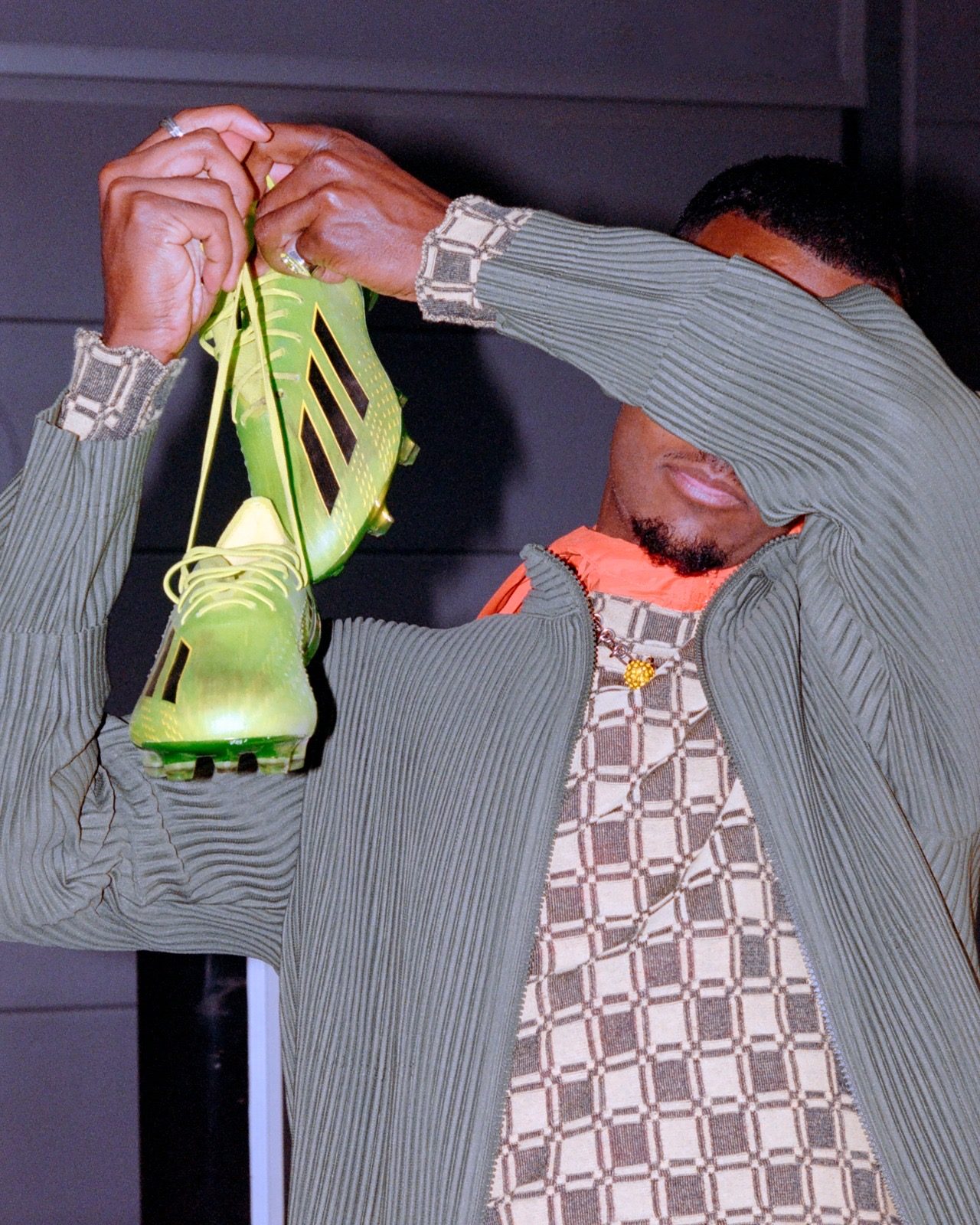 Alexander Isak holding a pair of lime adidas boots up by the laces, his face hidden behind his arm