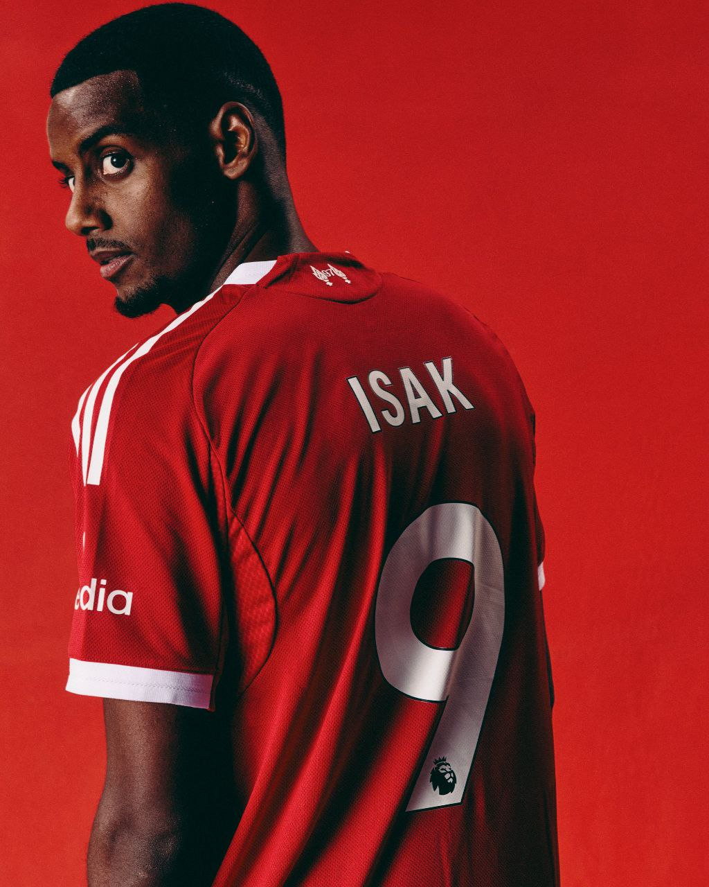 Alexander Isak against a red backdrop, seen from behind in a number 9 shirt, looking over his shoulder
