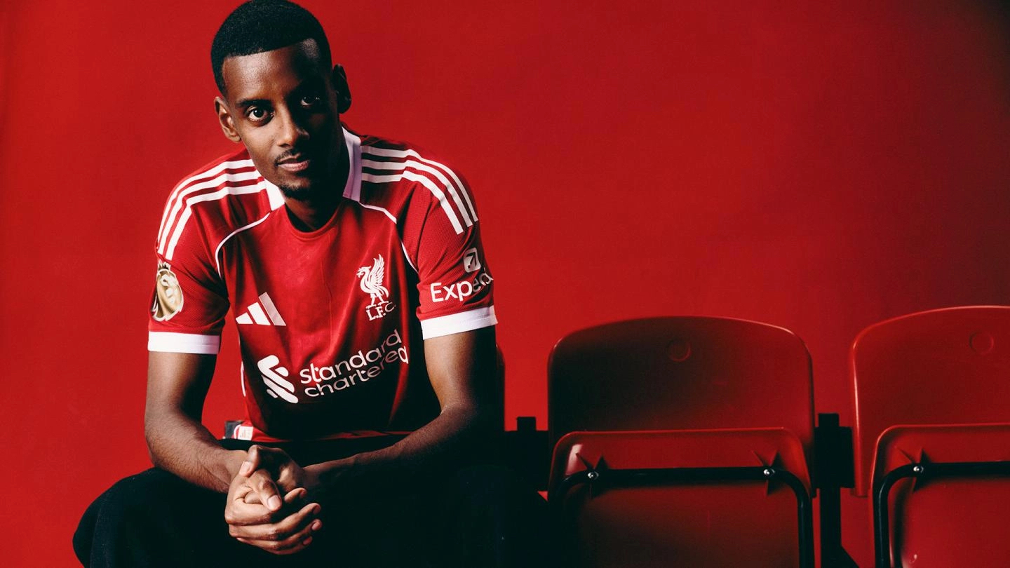 Alexander Isak in a red football shirt, seated beside red stadium seats against a red backdrop